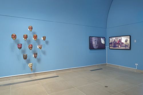 A triangle pattern of masks displayed against a blue wall, next to two monitors in the corner