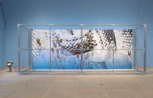 A chainlink fence around a display of masks, set against a snakeskin pattern