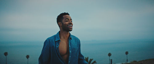 A young man in a blue shirt stands before the ocean