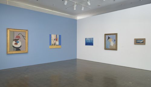 Two facing gallery walls, one blue and one white, with paintings hanging on them