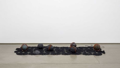 Round, lumpy forms are arranged on top of a dark textile on the floor