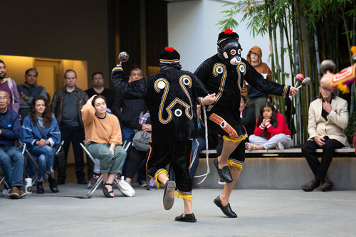 Two dancers in monkey costumes and masks link arms