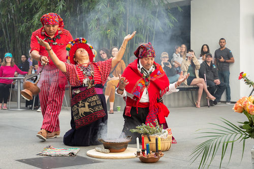 Two dancers kneel while one passes behind them with incense