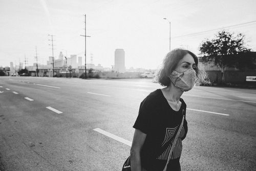 A black-and-white photo of a woman wearing a mask walking on an empty street