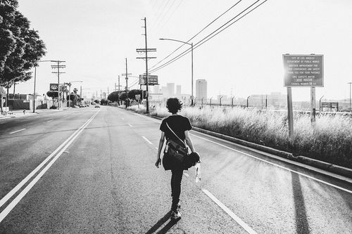 A black-and-white image of a woman walking away down an empty street