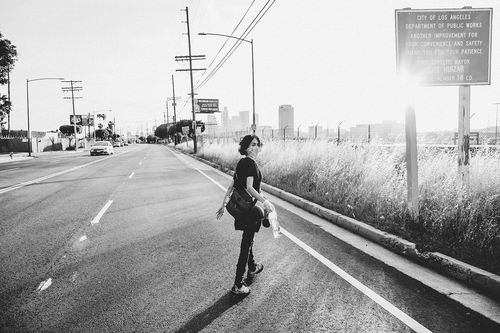 A black-and-white photo of a woman in a mask walking on an empty street