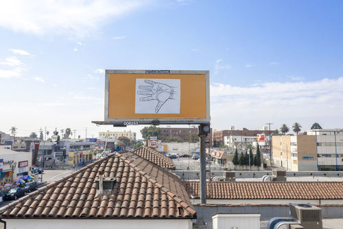 View over rooves of a city with clay tiled rooves. A billboard sign above the rooves has a graphic image of a palmistry diagram pasted on a gold background. 