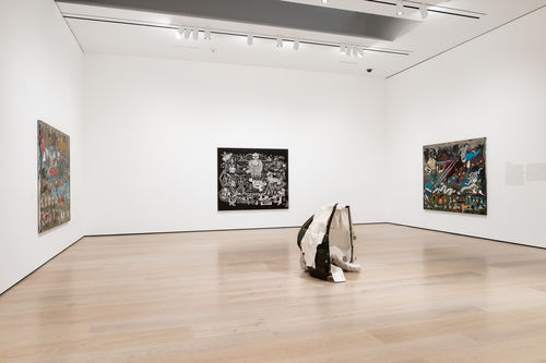 Gallery installation view showing a corner of a gallery painted in white with two paintings on the left and right walls, and a conical sculpture in the foreground