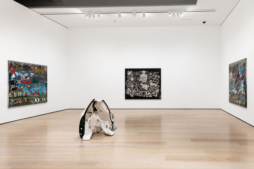 Gallery installation view showing a corner of a gallery painted in white with two paintings on the left and right walls, and a conical sculpture in the foreground
