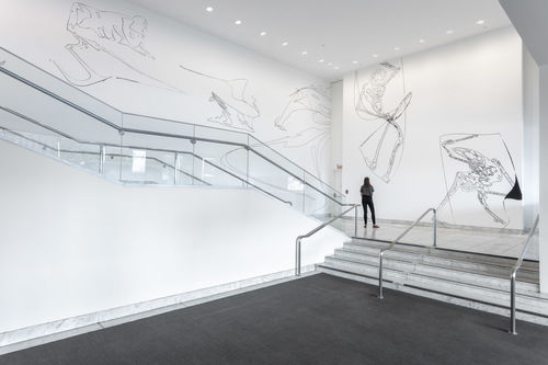 A large staircase, with tall white walls covered in thin black figures