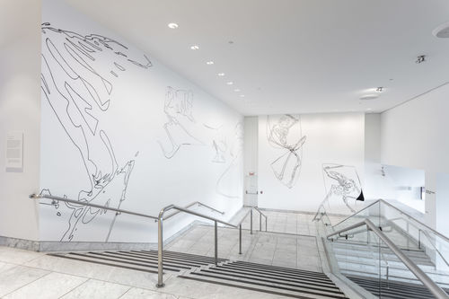 A large staircase, with tall white walls covered in thin black figures