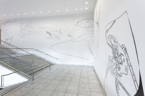 A large staircase, with tall white walls covered in thin black figures