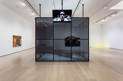 A large, mirror-like cube in the middle of a gallery, with television screens along each side