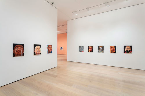 A view of a gallery where several small portraits hang