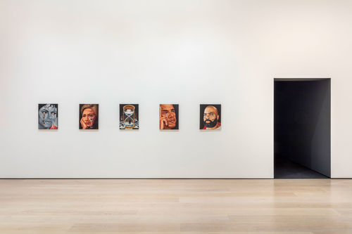 A view of a gallery where several small portraits hang