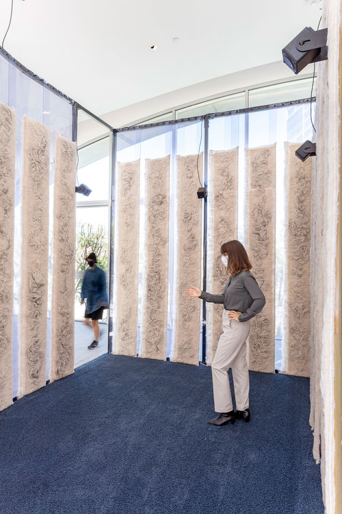 Inside a structure with plastic walls covered in strips of tan fiber, with two women passing through