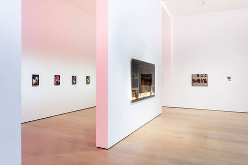 A view of a gallery with a floating wall in the middle, where a lightbox collage hangs