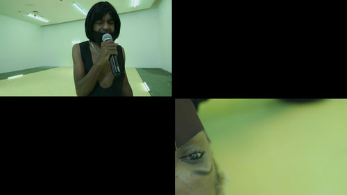 A rectangular image is split evenly into four quadrants. In the top left a figure with dark skin, a black shirt and  black hair holds  a microphone to the mouth. IN the background a room with fluorescent lights and a yellow floor is visible. In the lower quadrant, half of a dark-skinned face wearing a face mask is visible upside-down on the left. The other two quadrants are black.