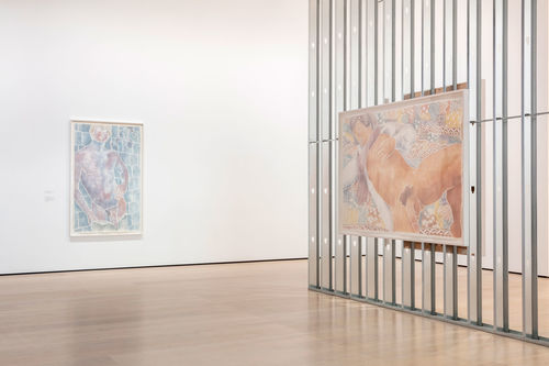 An exposed wall in a gallery with a large woodcut of a man hanging on it, and a white wall with another woodcut displayed