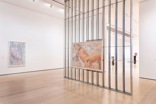 An exposed wall in a gallery with a large woodcut of a man hanging on it, and a white wall with another woodcut displayed