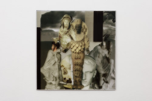 Square image hung on a wall with a collage of dark imagery, some on transparent material, including ancient Greek statues, a skill, Egyptian sculpture, a modern women's face.