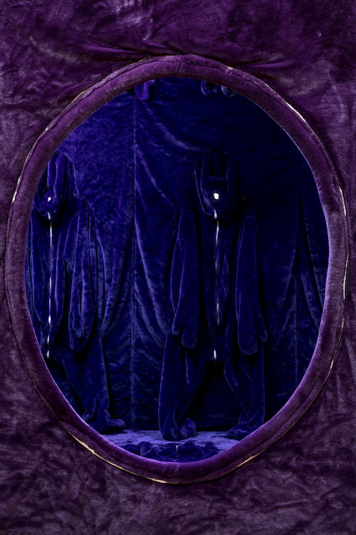 A vertical image shows a circular opening in a wall, looking into a chamber. The wall and chamber are covered in a purple velvet material.