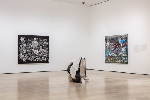 Gallery installation view showing a corner of a gallery painted in white with two paintings on the left and right walls, and a conical sculpture in the foreground