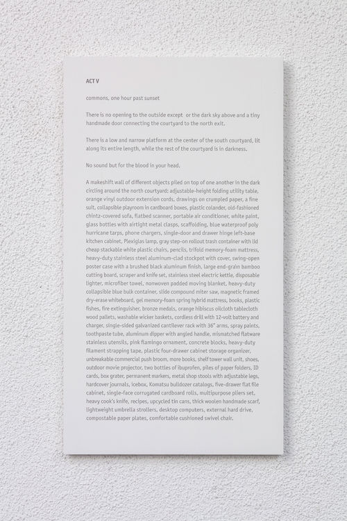 Photo of an exhibition label on a white wall with grey text on a white background.