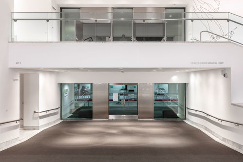 Image of the Hammer Lobby, looking towards glass doors in the background, a balcony is visible above the doors with open double-hung doors on the balcony. On the white surface of the balcony the words "ACT I" appear at upper left in thin grey letters, and on the right are the words "YOUNES & SORAYA NAZARIN LOBBY"