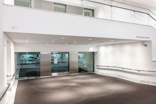 Image of the Hammer Lobby, looking towards glass doors in the background, a balcony is visible above the doors with open double-hung doors on the balcony. On the white surface of the balcony the words "ACT I" appear at upper left in thin grey letters, and on the right are the words "YOUNES & SORAYA NAZARIN LOBBY"