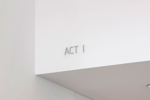 View of white walls and an architectural overhang, with the words "ACT I" set in thin grey three-dimensional letters on the overhang. 