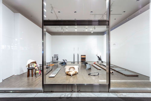 View looking into a room through a glass wall and glass doors. The room has various objects sitting on the floor.