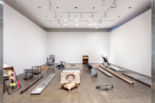 View of a room with white walls and a dark floor, with various objects sitting on the floor. 