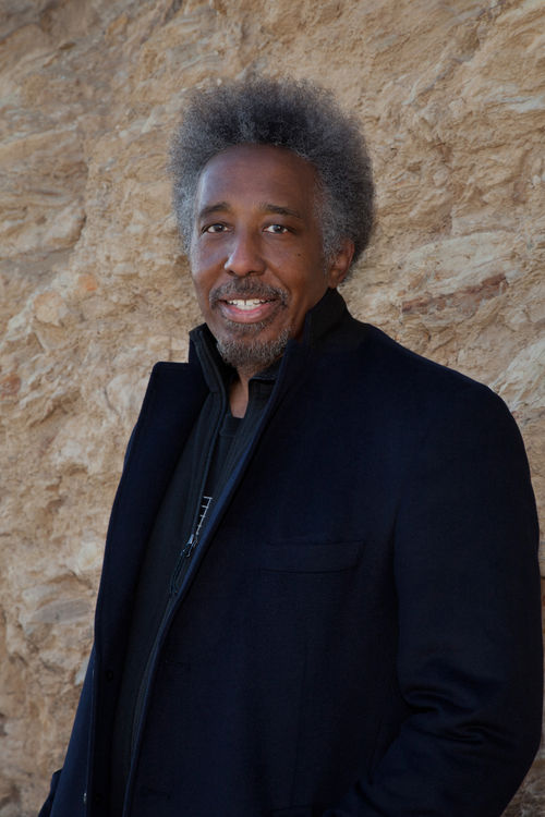 A photo portrait of a man in a black peacoat against a tan wall