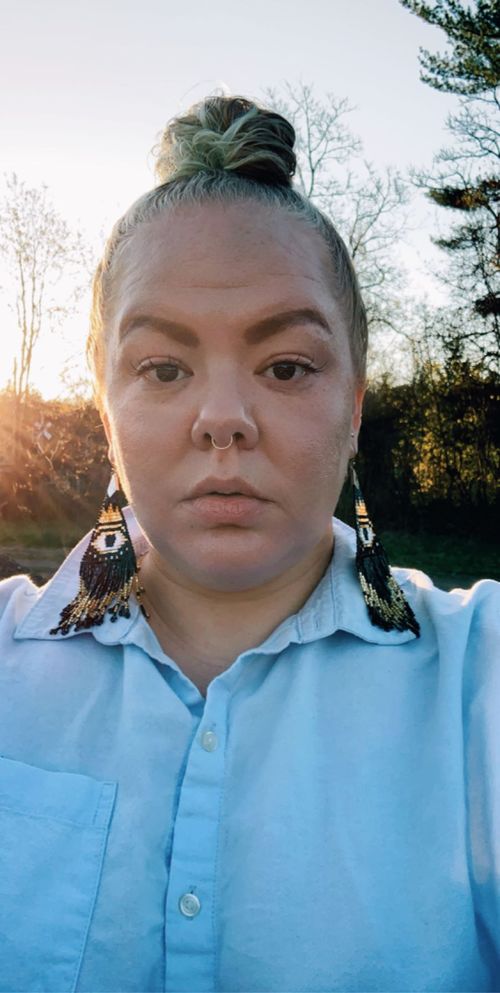 A photograph of a woman in a blue collared shirt with large earrings