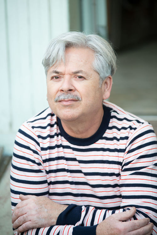 A man in a striped shirt poses with his arms crossed
