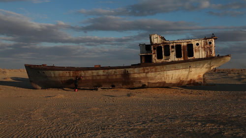 Photo of a worn, whiite boat sitting atop brown earth with a blue sky and cloudsin the background.