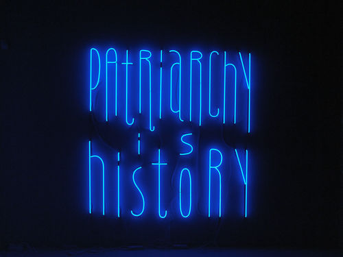 A blue neon sign which reads Patriarchy is History