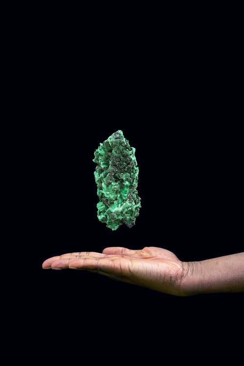 A green rock floats above an outstretched hand against a black background