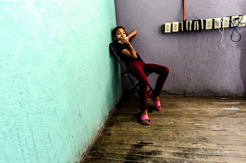 A young child sits in a corner next to a big teal wall