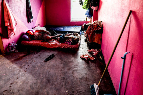A woman lays on a mattress on the floor of a pink room