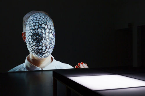 A figure with a jeweled face on a screen before a white platform