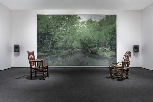 Two wooden chairs sit in the same room as David Hartt's painting