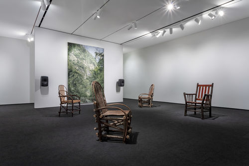 Four wooden chairs sit in the same room as David Hartt's painting