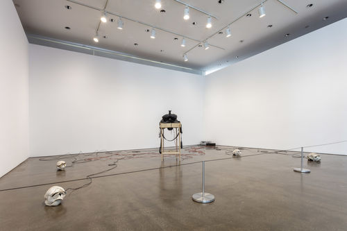 Horse saddle on wooden table connected to several skulls made of baseball leather