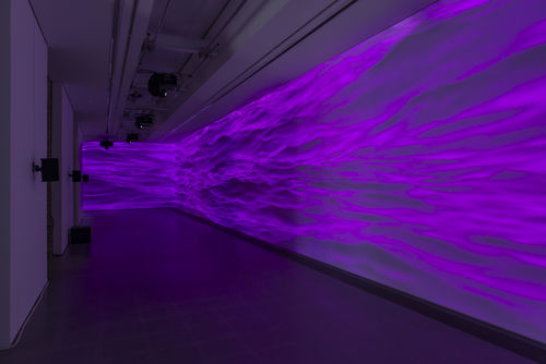 Projection of purple smoke texture runs along side a large wall in a dark room