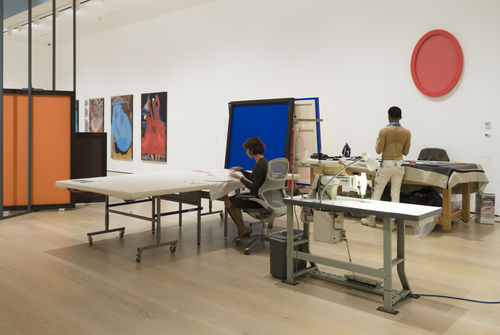 Two people are working on tables with fabric in an art gallery space. 