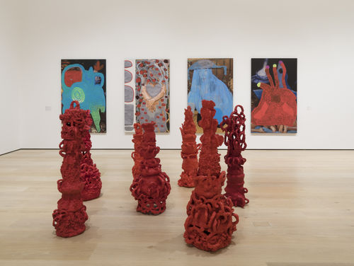 Gallery space with four abstract paintings on the wall and several red, curly-formed sculptures on the ground. 