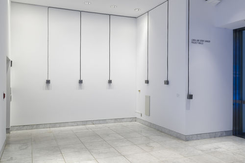 Five small speakers are attached to two white walls in a museum lobby.