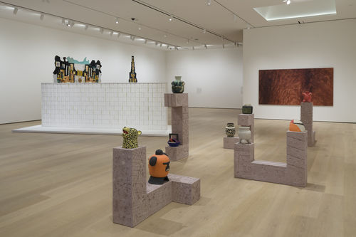 Gallery space with a set of rectangular shaped structures in the foreground, with colorful ceramic creatures on top of them.